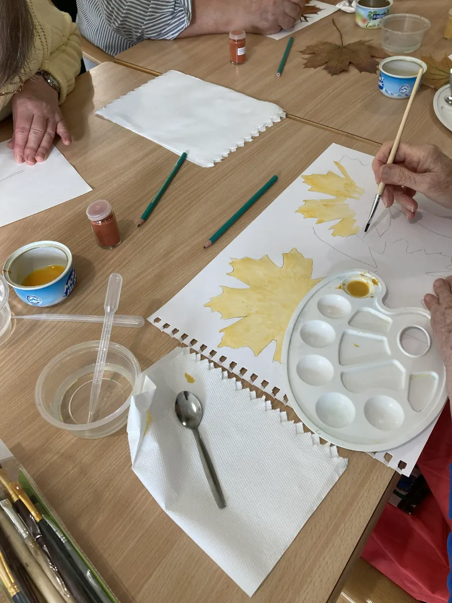 Participants peignant des feuilles d'automne à l'aquarelle autour d'une table, avec palette et pinceaux